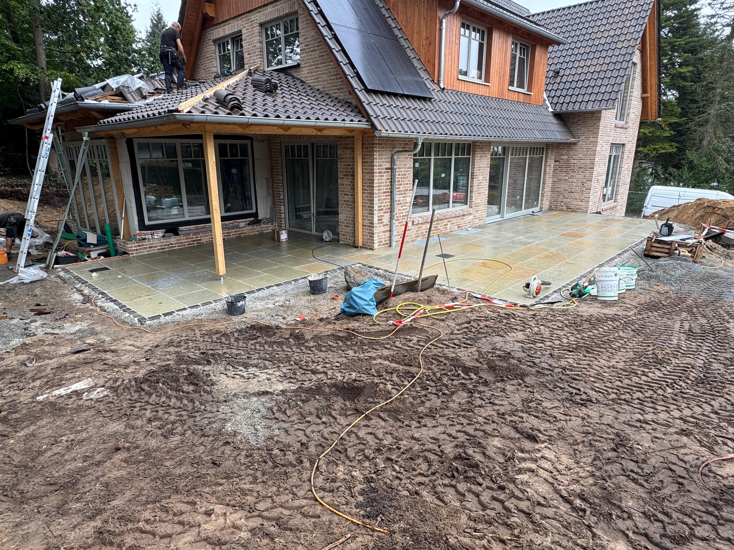 Neue Natursteinterrasse an Neubau mit Dacharbeiten, Baustelle im Garten- und Landschaftsbau